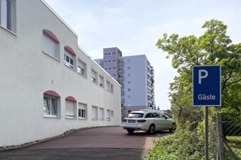 Au&szlig;enansicht des Hotel am Westend mit Parkfl&auml;che f&uuml;r G&auml;ste und angrenzendem Wohngeb&auml;ude unter blauem Himmel.