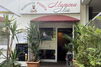 Der Eingang des Ristorante Pizzeria Mamma Mia mit Pflanzen davor, als Teil des Hotel am Westend Komplexes in einer urbanen Umgebung.