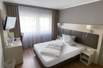 Gem&uuml;tliches Hotelzimmer im Hotel am Westend mit einem gro&szlig;en Bett, Holzfu&szlig;boden und einem Schreibtisch mit Fernseher und Ventilator