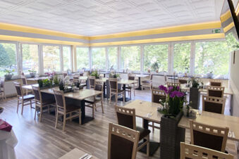 Helles und freundliches Restaurant mit gro&szlig;en Fenstern und dekorativen Pflanzen im Hotel am Westend mit Sitzgelegenheiten f&uuml;r G&auml;ste.