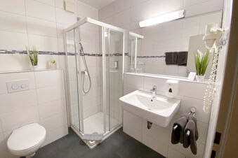 Helles und modernes Badezimmer mit Dusche, Waschbecken und WC im Hotel am Westend, ausgestattet mit Handt&uuml;chern und Pflanzen.
