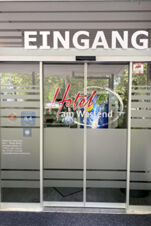 Automatische Glast&uuml;r am Eingang des Hotel am Westend mit Beschriftung und Sicht auf B&auml;ume drau&szlig;en, modernes Design sichtbar