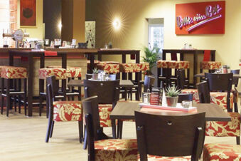Gem&uuml;tlicher Restaurantbereich mit Holzst&uuml;hlen und roten, gemusterten Polstern im Hotel am Westend, warme Beleuchtung und moderne Einrichtung.