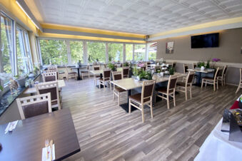Helles und moderner Restaurantbereich mit Holzboden und gro&szlig;en Fenstern im Hotel am Westend, dekoriert mit Pflanzen und Tafeln.