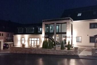 Nočn&iacute; pohled na osvětlen&yacute; exteri&eacute;r hotelu Landgasthof Niebler s modern&iacute;m hlavn&iacute;m vchodem a okrasn&yacute;mi rostlinami před budovou.