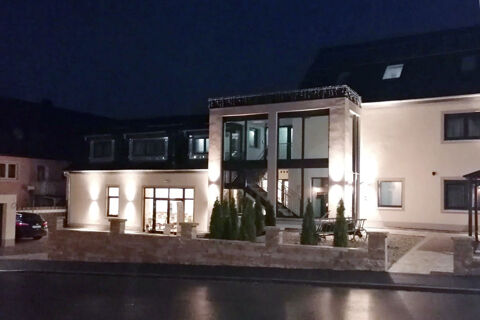 Nočn&iacute; pohled na osvětlen&yacute; exteri&eacute;r hotelu Landgasthof Niebler s modern&iacute;m hlavn&iacute;m vchodem a okrasn&yacute;mi rostlinami před budovou.