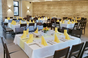 Elegantn&iacute; restaurace v hotelu Landgasthof Niebler s prostřen&yacute;mi stoly, žlut&yacute;mi ubrousky a kamenn&yacute;mi stěnami.