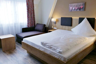 Moderně zař&iacute;zen&yacute; pokoj s postel&iacute;, pohovkou, dřevěn&yacute;m n&aacute;bytkem a z&aacute;věsy v hotelu Landgasthof Niebler, &uacute;tuln&yacute; a světl&yacute;.