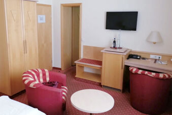 &Uacute;tuln&yacute; pokoj v hotelu Landgasthof Niebler s červen&yacute;mi křesly, TV na stěně a světl&yacute;m dřevěn&yacute;m n&aacute;bytkem v jednoduch&eacute;m designu.