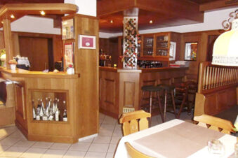 &Uacute;tuln&eacute; dřevěn&eacute; zař&iacute;zen&iacute; s barem a j&iacute;deln&iacute;mi stoly v restauraci hotelu Landgasthof Niebler s tepl&yacute;m osvětlen&iacute;m a v&yacute;zdobou.