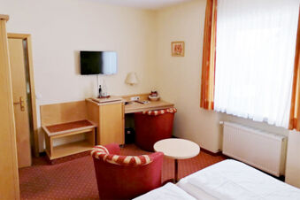 Gem&uuml;tlich eingerichtetes Zimmer im Hotel Landgasthof Niebler mit zwei Betten, Fernseher, Tisch, St&uuml;hlen und gro&szlig;en Fenstern.