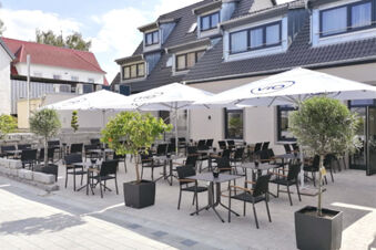 Venkovn&iacute; prostor s několika stoly, židlemi a slunečn&iacute;ky před hotelem Landgasthof Niebler za slunečn&eacute;ho dne