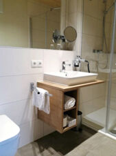 Modern&iacute; koupelna v hotelu Landgasthof Niebler s umyvadlem, ručn&iacute;ky, kosmetick&yacute;m zrcadlem a sprchov&yacute;m koutem ve světl&eacute;m designu.