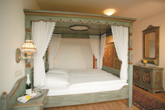 Bedroom in Burg-Hotel Obermoschel with wooden four-poster bed, white curtains, nightstand with lamp and bottle with glasses