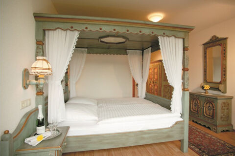 Bedroom in Burg-Hotel Obermoschel with wooden four-poster bed, white curtains, nightstand with lamp and bottle with glasses