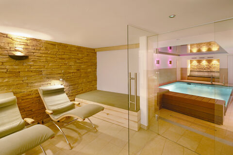 Indoor pool area with lounge chairs and a cushioned bench in Burg-Hotel Obermoschel with stone wall and glass door entrance