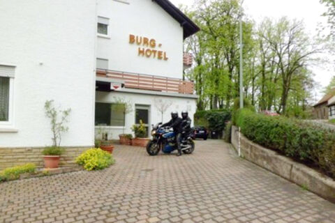 White building with balconies and brown letters reading Burg-Hotel Obermoschel, two bikers on a motorcycle outside