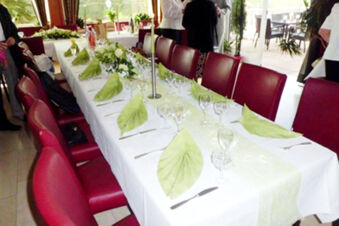 Long table set for dining with white tablecloth, green napkins, glassware, and red chairs at Burg-Hotel Obermoschel