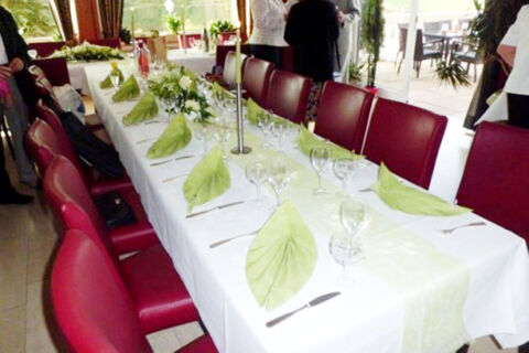 Long table set for dining with white tablecloth, green napkins, glassware, and red chairs at Burg-Hotel Obermoschel