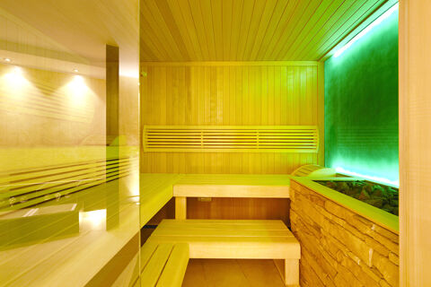 Interior of a wooden sauna with benches, stone heater, green illuminated wall, and glass door at Burg-Hotel Obermoschel