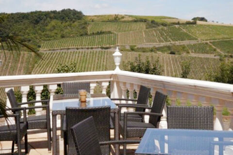 Outdoor terrace seating with glass tables and black wicker chairs overlooking vineyard hills at Burg-Hotel Obermoschel