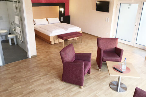 Hotel room at Burg-Hotel Obermoschel featuring a bed with two pillows, two red armchairs, a small table, and a bathroom visible through a door