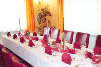 Dining table set with folded burgundy napkins, glassware, and cutlery in a bright room at Burg-Hotel Obermoschel