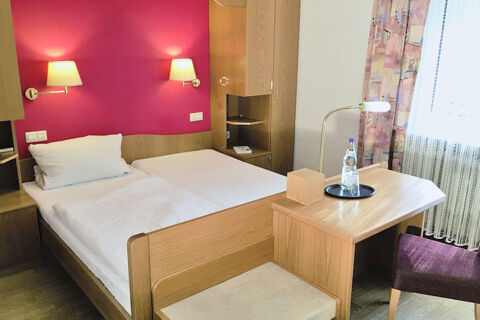 Hotel room at Burg-Hotel Obermoschel with twin beds, red accent wall, wood furniture, desk, chair, and a bottle of water on tray
