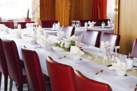 Dining room with white tablecloths, napkins, floral centerpieces and red chairs at Burg-Hotel Obermoschel