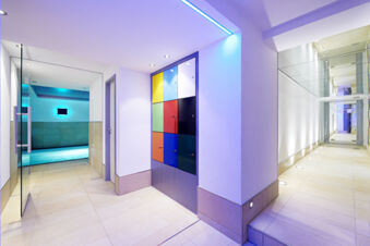 Modern spa area hallway with colorful lockers, glass doors, and a lit indoor pool at Burg-Hotel Obermoschel