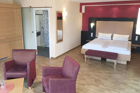 Hotel room at Burg-Hotel Obermoschel with double bed, burgundy armchairs, wooden flooring, and open bathroom door visible