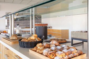 Various breads, croissants, pastries, cake, and milk containers displayed on a self-serve counter at B&B Hotel Cherasco Langhe