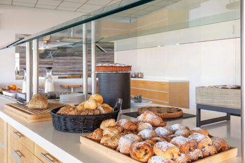 Various breads, croissants, pastries, cake, and milk containers displayed on a self-serve counter at B&B Hotel Cherasco Langhe