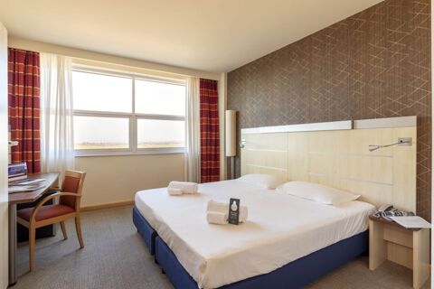 Clean hotel room at B&B Hotel Cherasco Langhe with twin beds, bedside table, desk, chair, large window, and curtains
