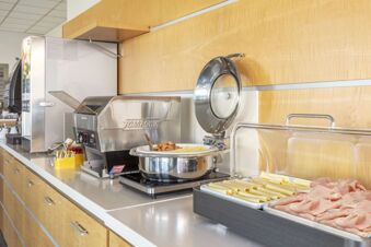 Breakfast buffet setup with toast machine, coffee dispenser, scrambled eggs, pastries, and sliced meats at B&B Hotel Cherasco Langhe