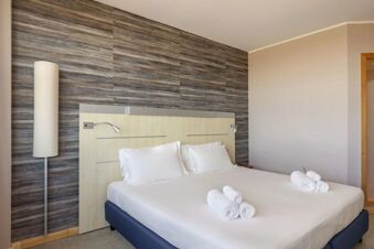 Bed with white linens and pillows, a wooden headboard, rolled towels, and a tall floor lamp at B&B Hotel Cherasco Langhe