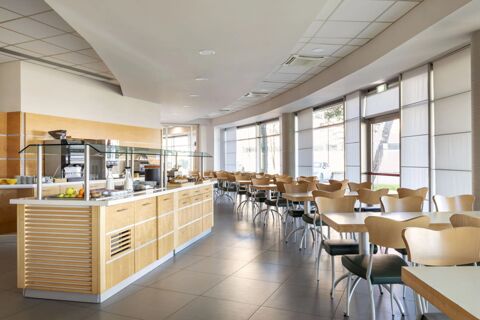 Bright dining area with wooden chairs, tables, a breakfast counter with pastries, and large windows at B&B Hotel Cherasco Langhe