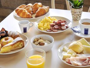Breakfast spread with croissants, scrambled eggs, sliced sausages, cereal, cheese, cold cuts, orange juice, and coffee at B&B Hotel Imperia Rossini al Teatro