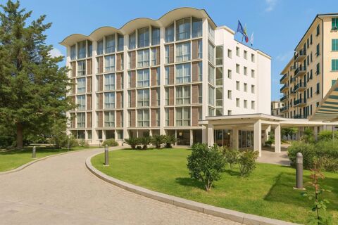 Modern multi-story building with large windows and a curved roof next to a curved walkway and green lawns at B&B Hotel Imperia Rossini al Teatro