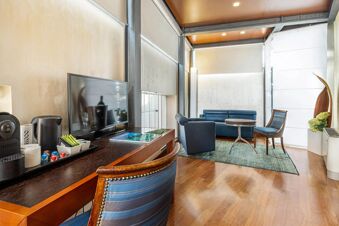 Living area of B&B Hotel Imperia Rossini al Teatro with blue armchairs, a round table, flatscreen TV, and coffee machine on a wooden desk