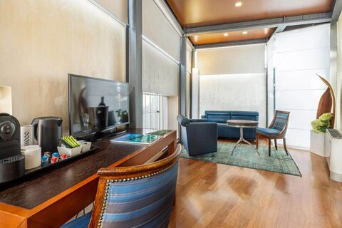 Living area of B&B Hotel Imperia Rossini al Teatro with blue armchairs, a round table, flatscreen TV, and coffee machine on a wooden desk