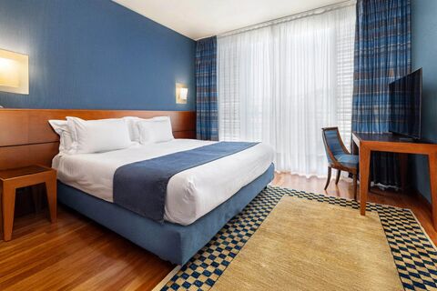 Hotel room at B&B Hotel Imperia Rossini al Teatro with blue walls, large bed, wooden furniture, and a TV on a desk