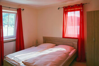 Bedroom at Rheinhotel Zum Anker with wooden double bed, white bedding, red curtains, window, nightstand, and wardrobe