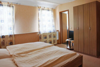 Double bed with beige bedding next to two windows with patterned curtains and a wardrobe inside Rheinhotel Zum Anker