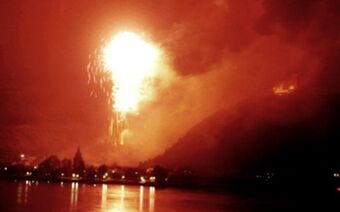 Ognjemet razsvetljuje noč nad rečno pokrajino v bližini hotela Rheinhotel Zum Anker z odsevom v vodi in hribi v ozadju.