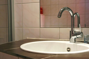 White sink with chrome faucet on brown countertop against tiled wall and mirror at Rheinhotel Zum Anker