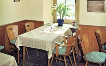 Small dining area with wooden chairs and table covered by white cloth near a window with plant in Rheinhotel Zum Anker