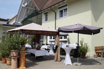 Outdoor dining area of Landgasthof Bieg with white tablecloths, a beige tent, a black umbrella, and several potted plants