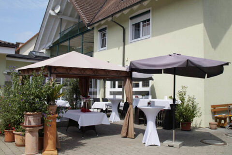 Outdoor dining area of Landgasthof Bieg with white tablecloths, a beige tent, a black umbrella, and several potted plants