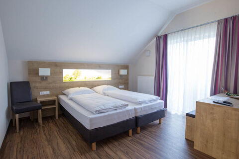A modern hotel room at Landgasthof Bieg with two single beds, wooden furniture, a chair, and a large window with curtains